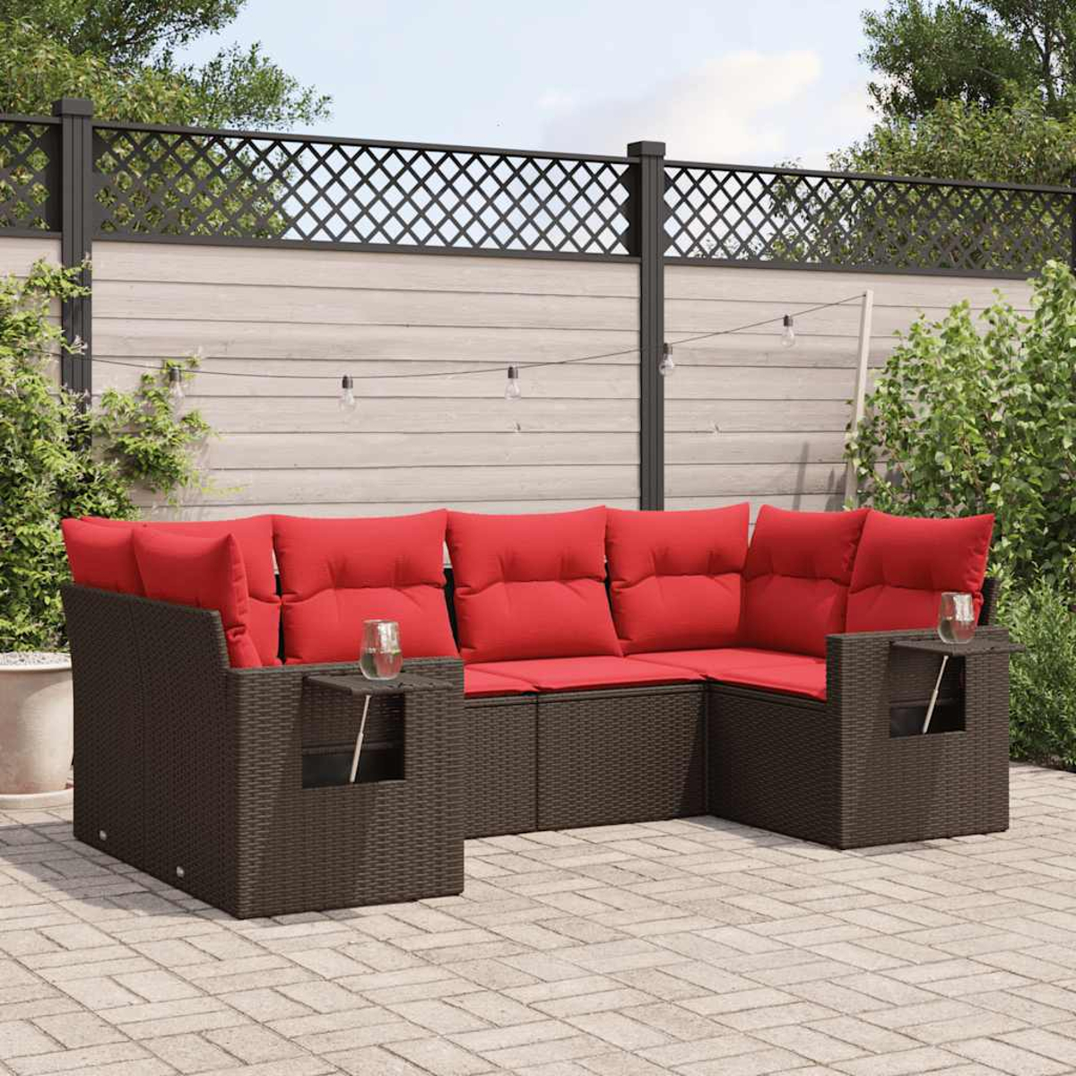 Outdoor-Ecksofa mit roten Kissen auf einer Ziegelterrasse. Ein Zaun und Pflanzen im Hintergrund. Gläser auf den Beistelltischen.