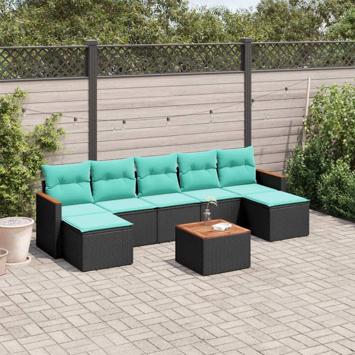 Outdoor-Ecksofa mit türkisfarbenen Kissen und einem hölzernen Couchtisch. Auf einer Ziegelstein-Terrasse, mit einem Zaun und Grün im Hintergrund.