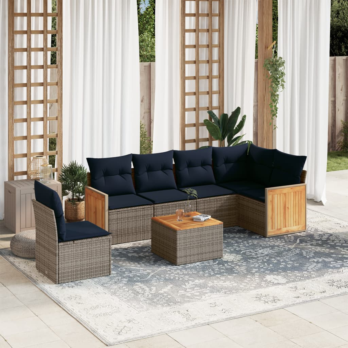 Juego de asientos al aire libre con cojines azul marino sobre una alfombra estampada. Incluye sofá, silla y mesa. Cortinas blancas y plantas al fondo.