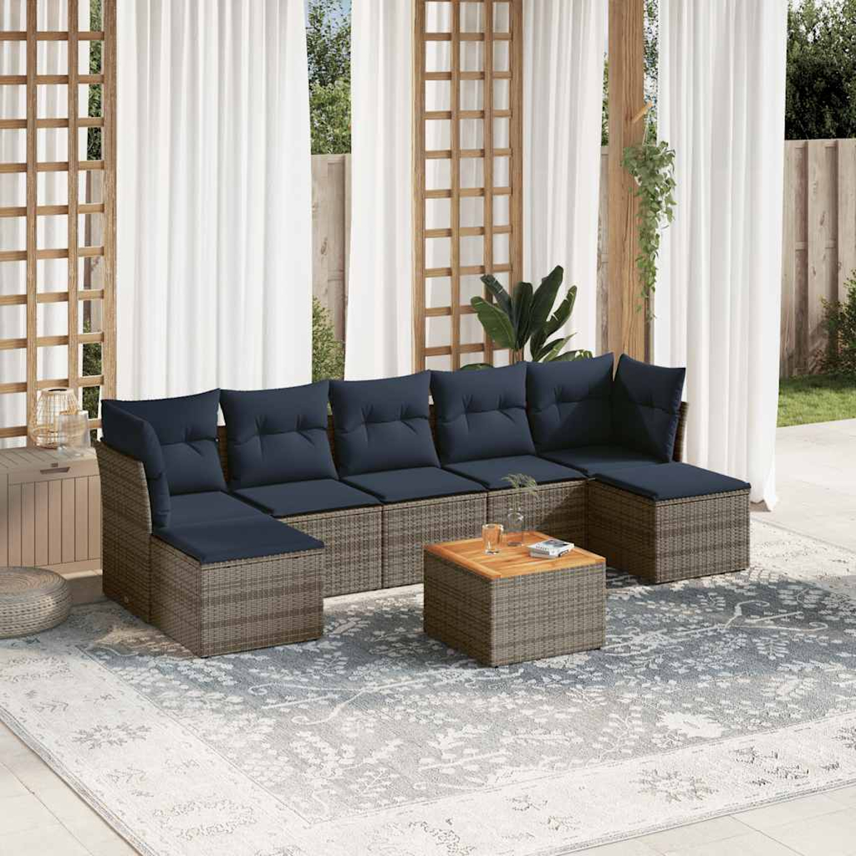 Outdoor-Ecksofa mit marineblauen Kissen und einem quadratischen Couchtisch auf einem gemusterten Teppich, vor weißen Vorhängen und Holzbalken.