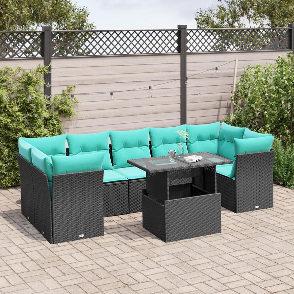 Garten-Sitzgruppe mit türkisfarbenen Kissen und einem Tisch mit Glasplatte. Auf einer Backstein-Terrasse, mit Holzzaun und Grün im Hintergrund.