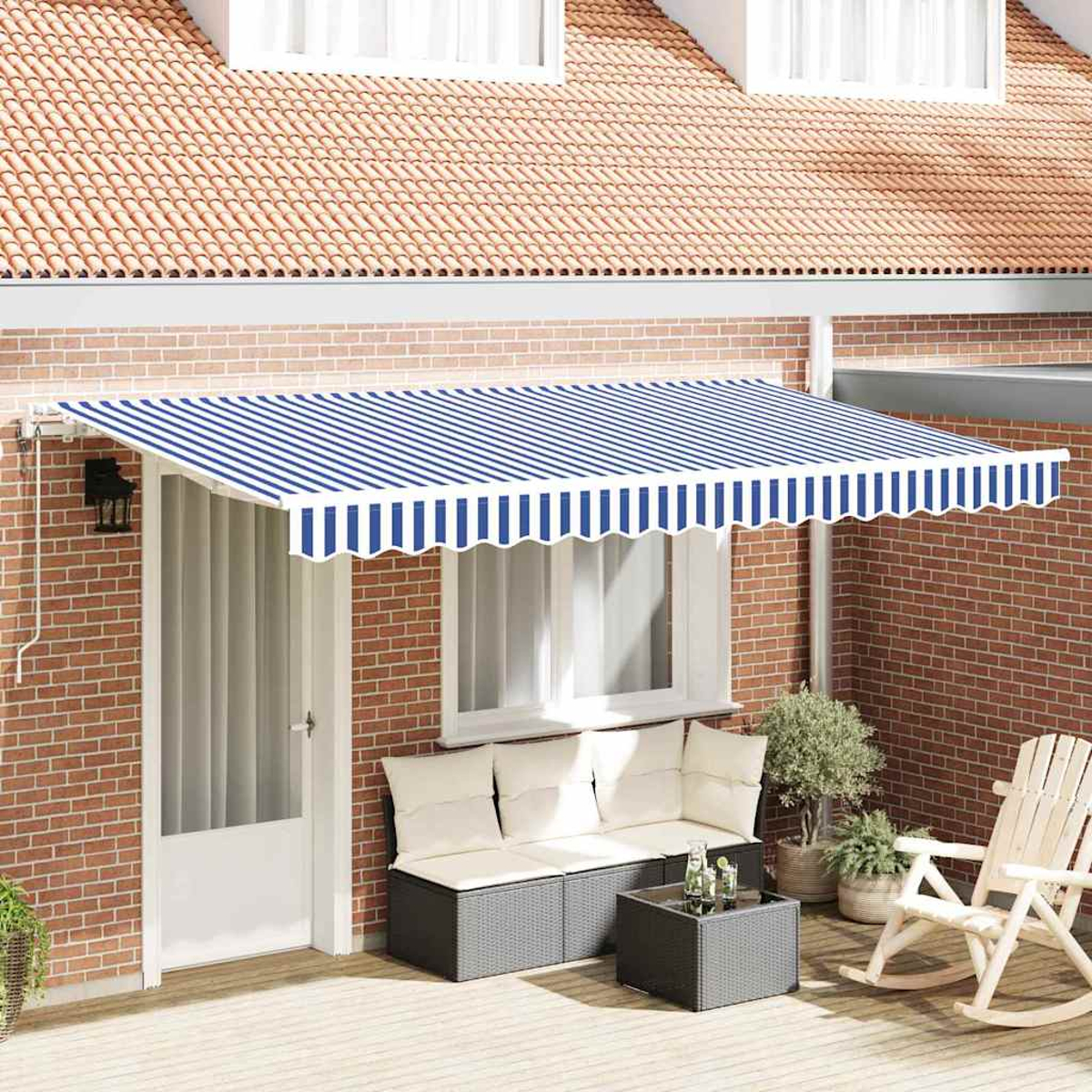 Eine Terrasse mit blau-weiß gestreifter Markise, weißer Tür, Sofa, Tisch mit Getränken, Schaukelstuhl und Pflanzen.
