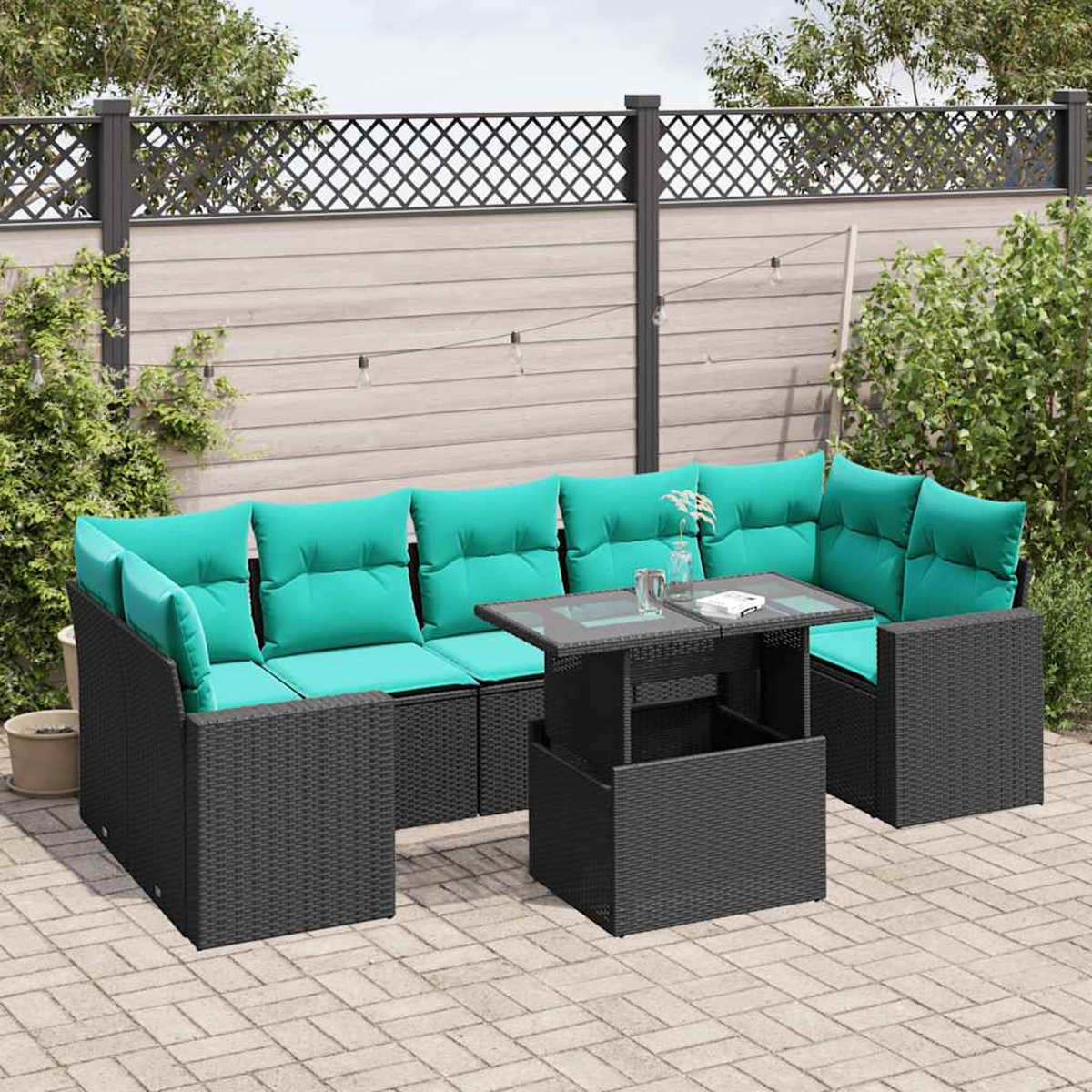 Terrassenmöbel-Set mit schwarzem Korbmöbeln, türkisfarbenen Kissen und einem Tisch mit Glasplatte. Auf einer Backstein-Terrasse mit Holzzaun im Hintergrund.