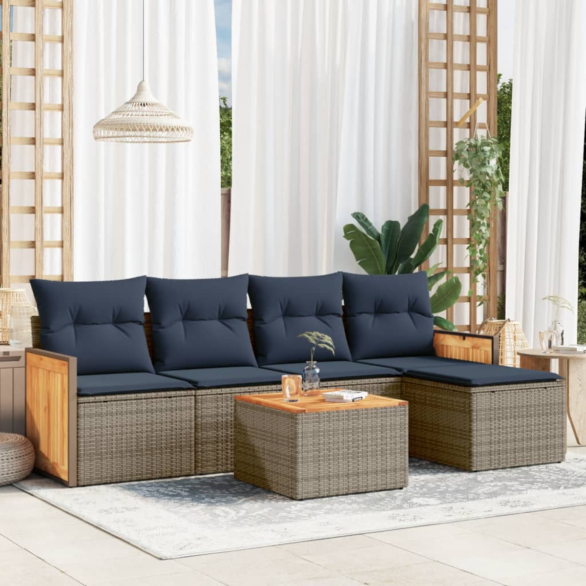 Gartenmöbel: Sofa mit blauen Kissen, Korbtisch und Teppich. Weiße Vorhänge und Pflanzen im Hintergrund.