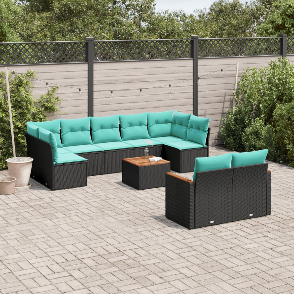 Juego de patio al aire libre con muebles de mimbre negro, cojines turquesa y una mesa de centro de madera. En un patio de ladrillos, rodeado de vegetación.