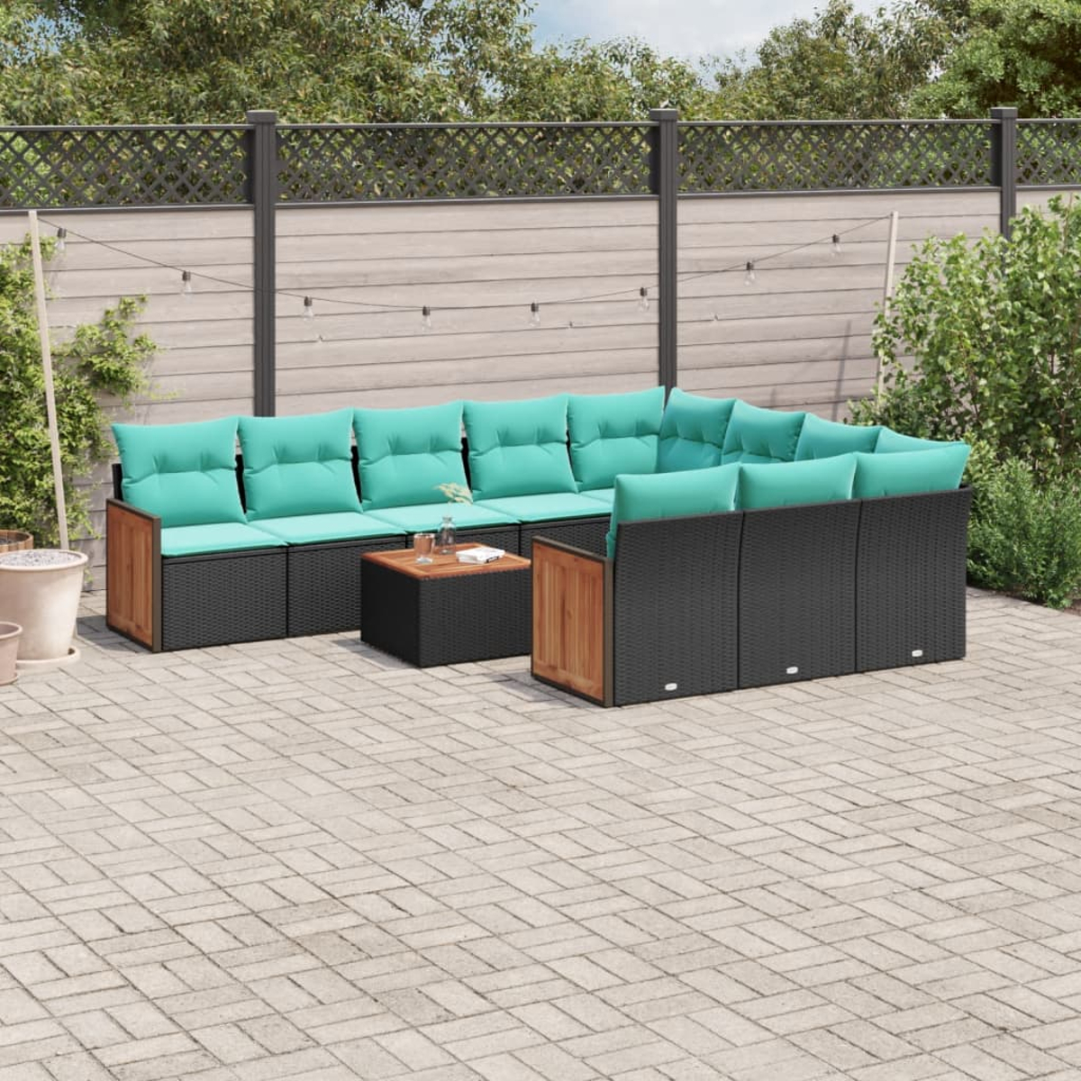 Outdoor-Ecksofa mit türkisfarbenen Kissen und einem Holztisch auf einer gepflasterten Terrasse. Im Hintergrund befinden sich ein Zaun und Grün.