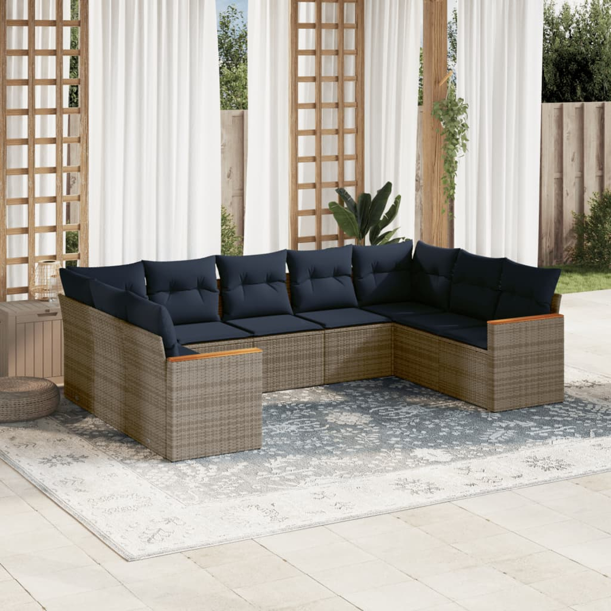 Außenszene mit einem geflochtenen Ecksofa mit marineblauen Kissen auf einem gemusterten Teppich und weißen Vorhängen.