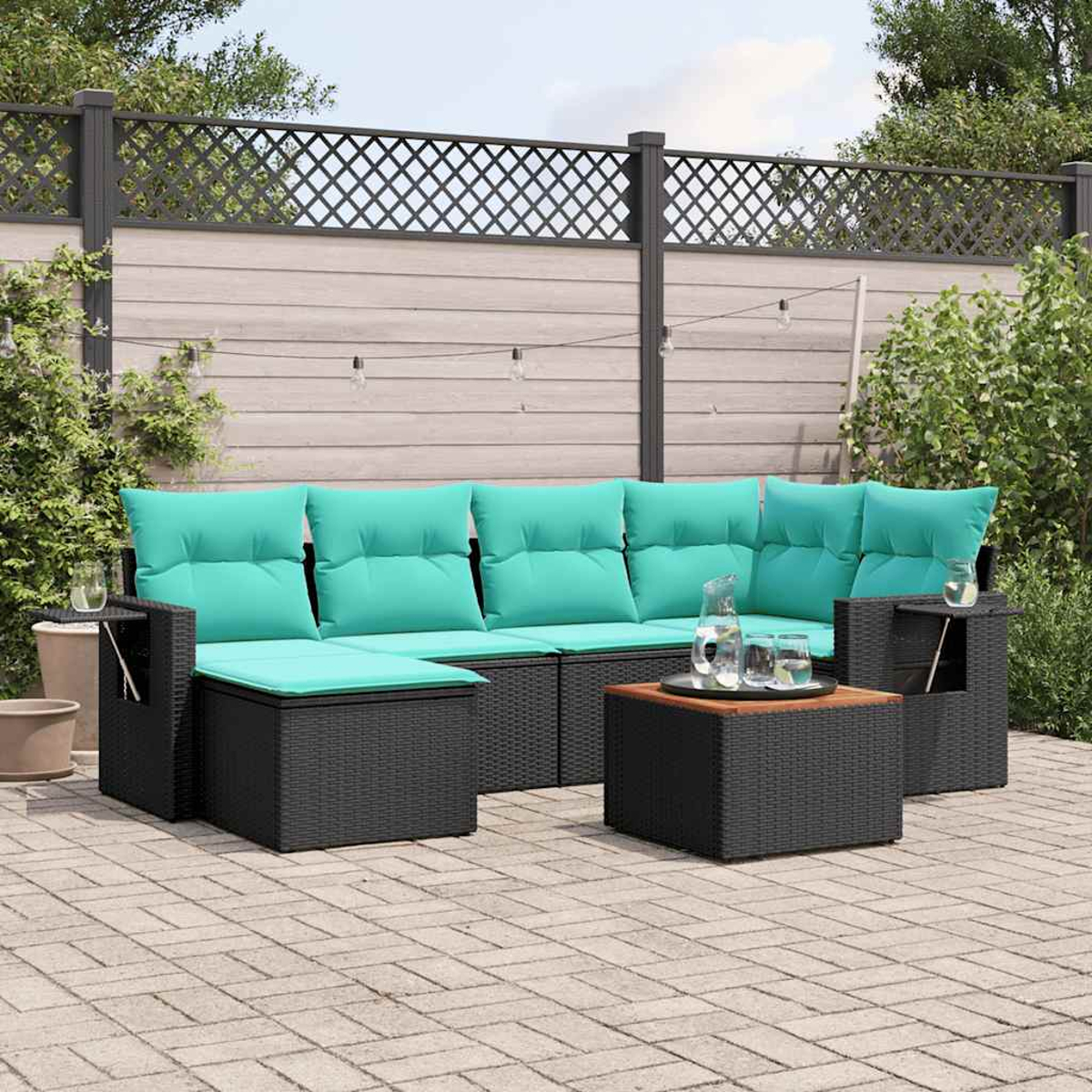 Gartensofa mit türkisfarbenen Kissen und schwarzem Korbboden. Davor ein kleiner Tisch und ein Couchtisch. Im Hintergrund ein Zaun.