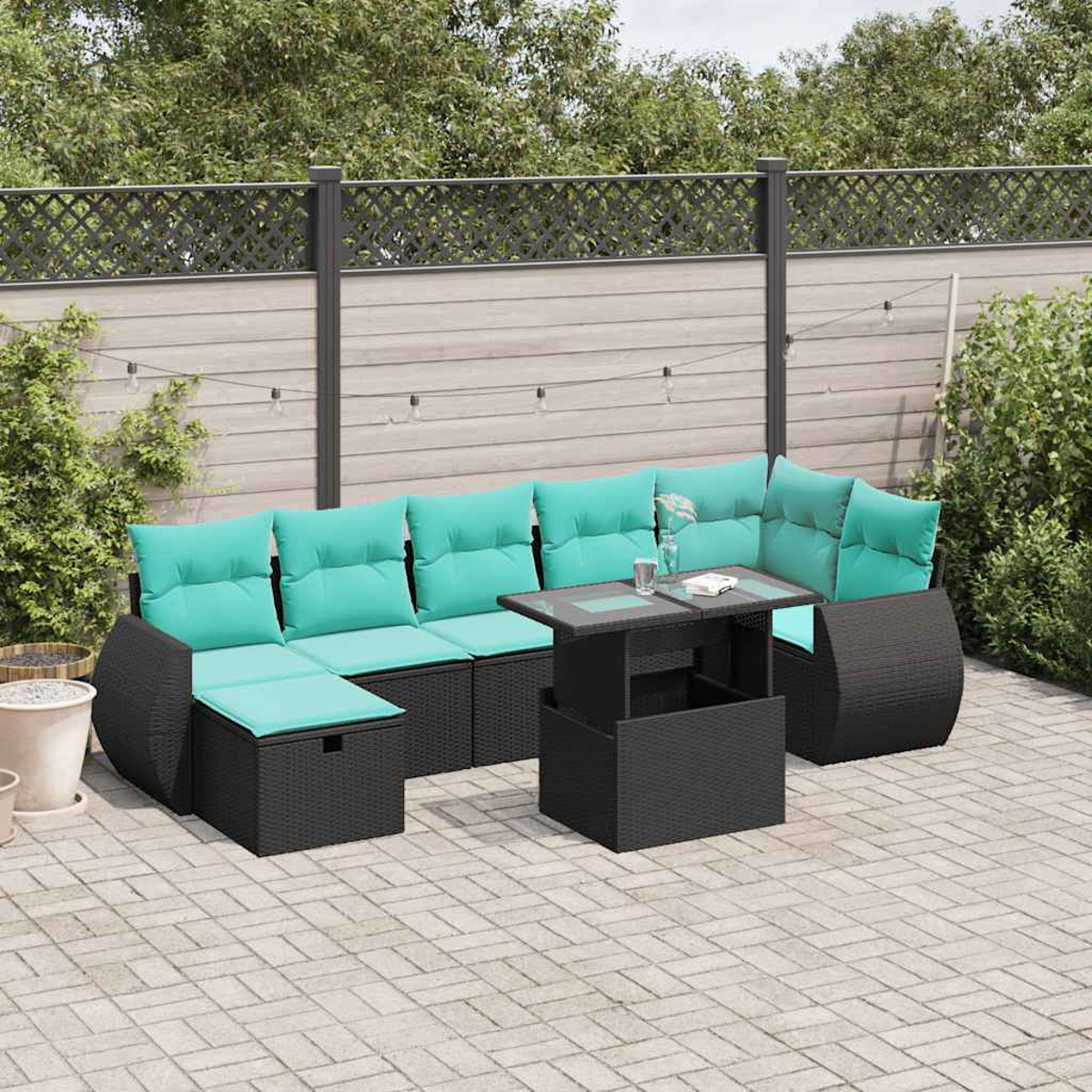 Gartensofa mit türkisfarbenen Kissen, schwarzem Tisch und Zaun im Hintergrund. Auf einer gepflasterten Terrasse.