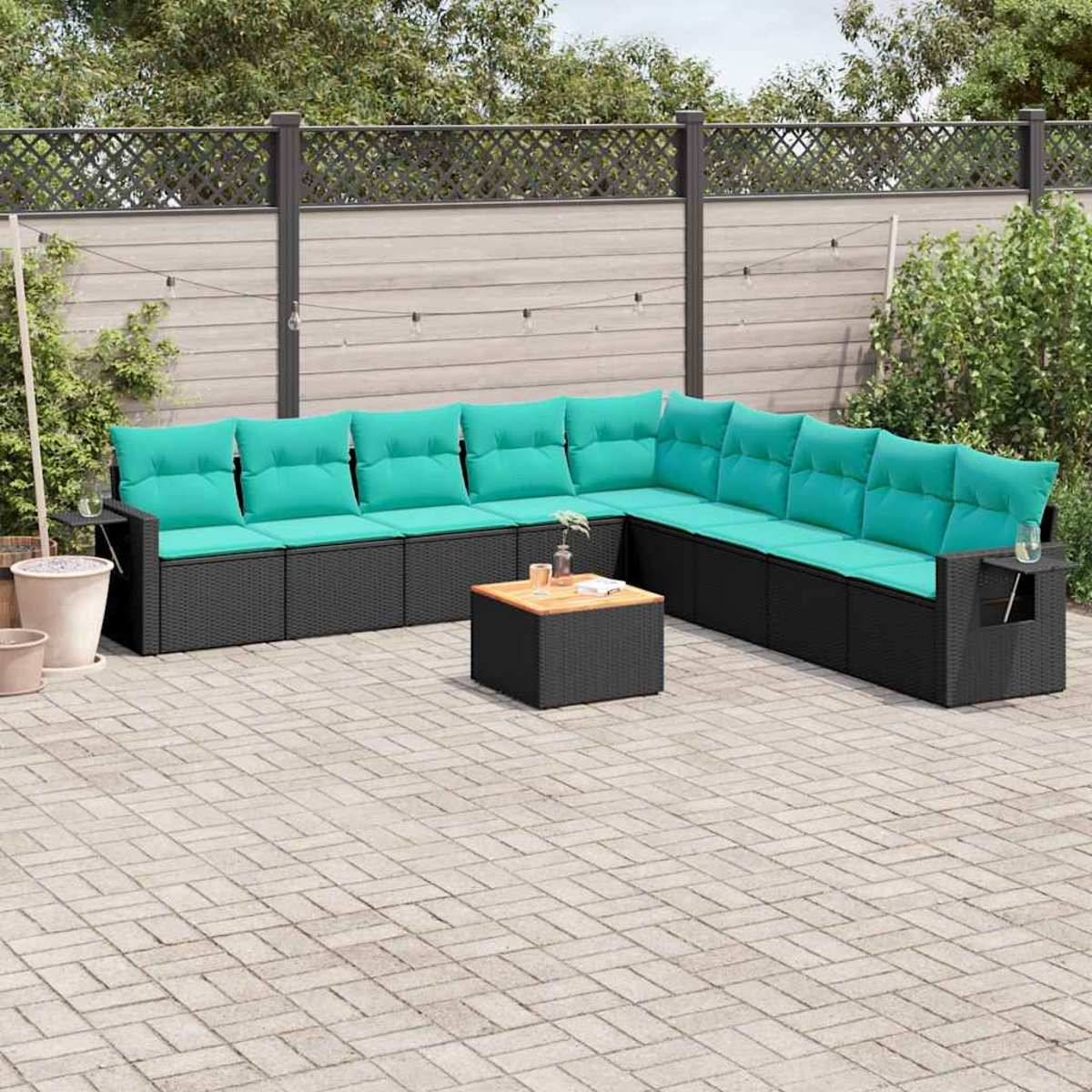 Outdoor-Ecksofa mit türkisfarbenen Kissen und einem kleinen Tisch auf einer Ziegelterrasse. Im Hintergrund ein Zaun und Grün.