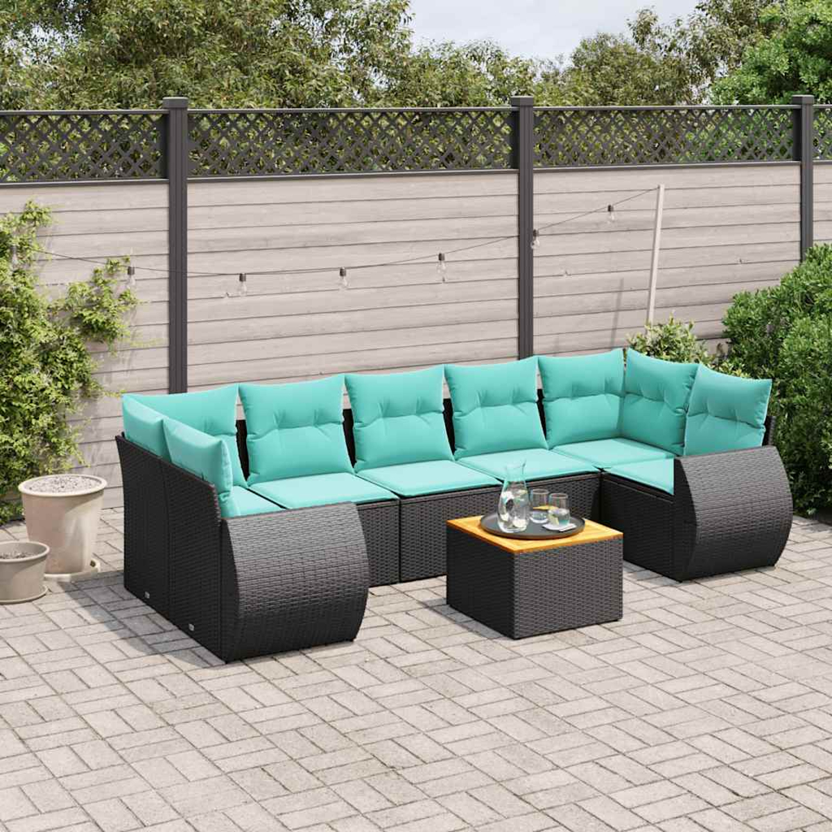 Gartensitzgruppe mit türkisfarbenen Kissen, einem kleinen Tisch und einem Zaun im Hintergrund. Die Sitzgruppe steht auf einer Ziegelterrasse.