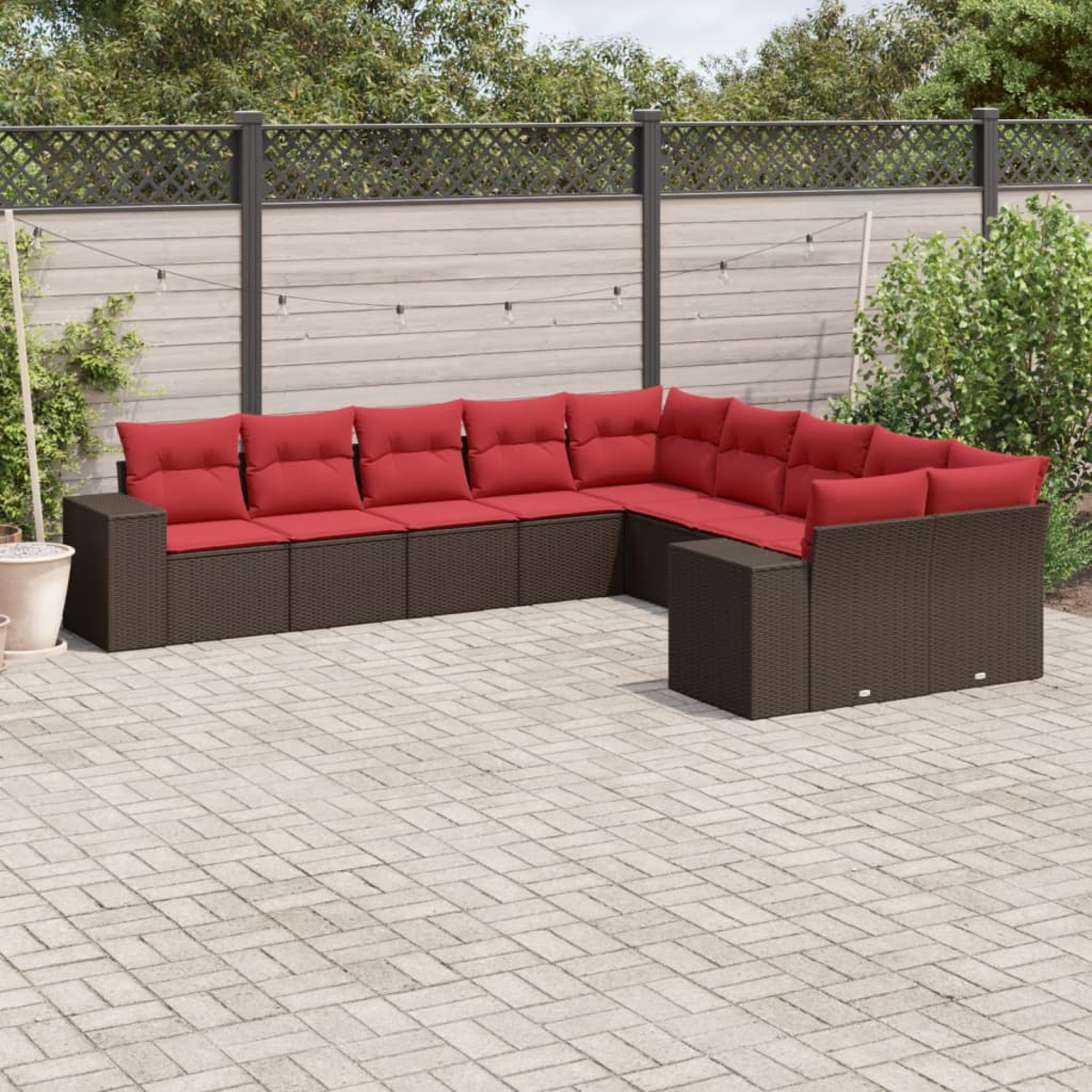 Ein Ecksofa mit roten Kissen im Freien steht auf einer Ziegelterrasse. Dahinter befinden sich ein Zaun, Pflanzen und eine Lichterkette.