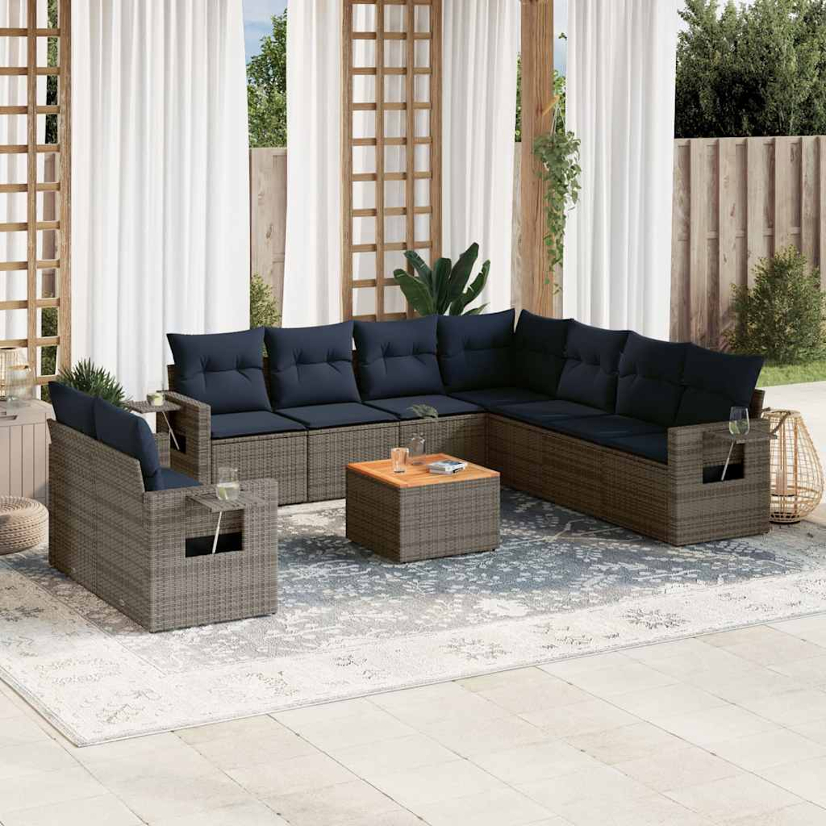 Outdoor-Sitzgruppe mit blauen Kissen. Enthält ein Ecksofa, Sessel und einen Couchtisch. Auf einem Teppich, mit weißen Vorhängen im Hintergrund.