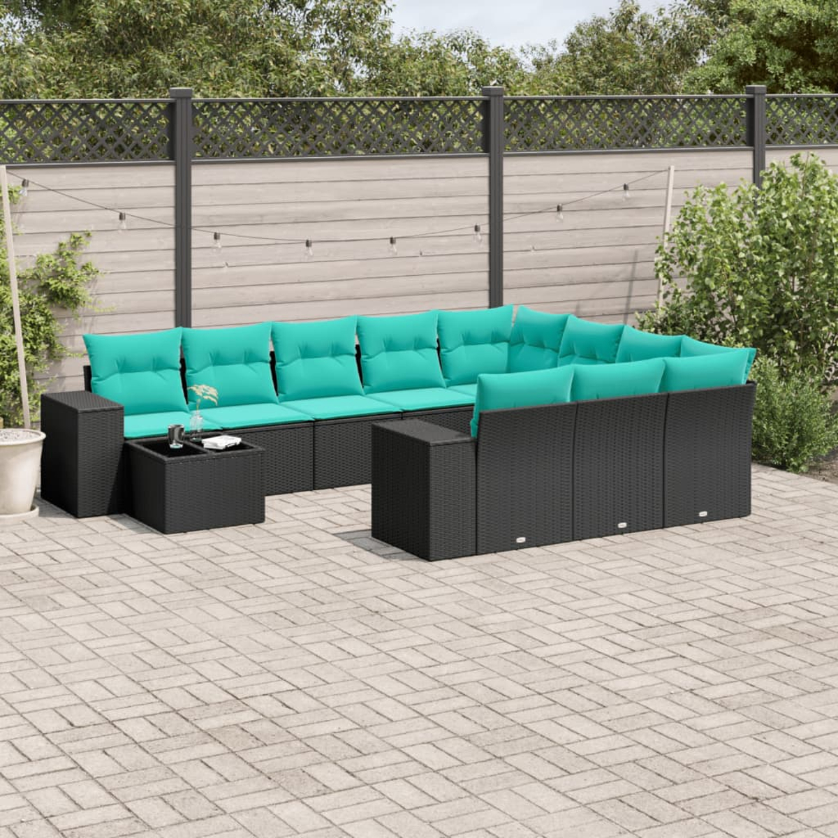 Juego de patio al aire libre con muebles de mimbre negro y cojines turquesa, en un patio pavimentado. Una mesita frente al sofá.