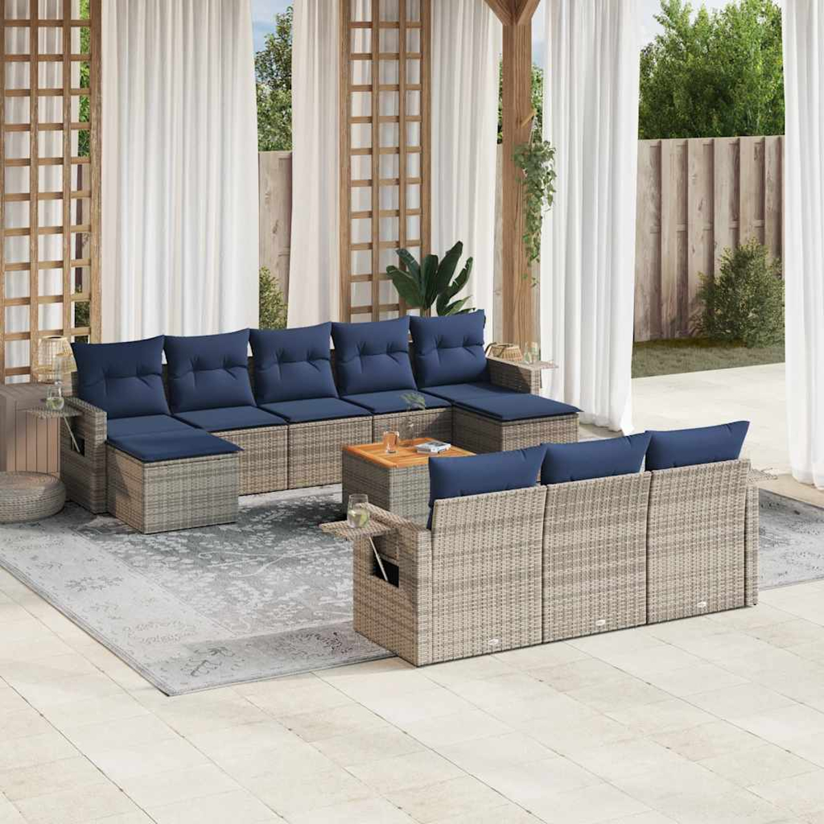 Outdoor-Sitzbereich mit grauen Rattan-Sofas und blauen Kissen. Zwischen den Sofas steht ein Holztisch. Weiße Vorhänge rahmen die Szene ein.