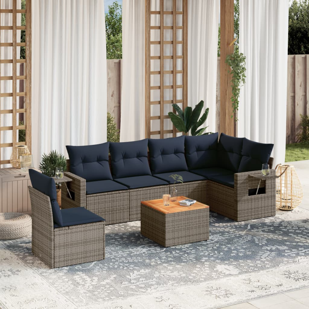 Outdoor-Terrassenset mit grauen Korbmöbeln, marineblauen Kissen und einem Couchtisch aus Holz auf einem blau gemusterten Teppich, weiße Vorhänge.