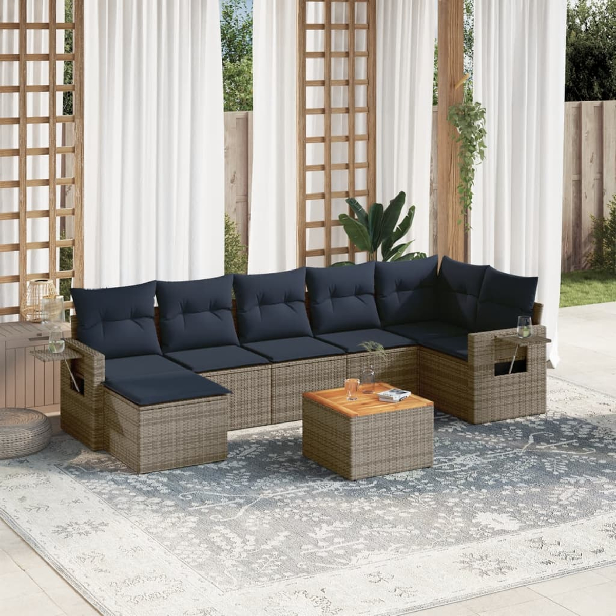 Ein Outdoor-Ecksofa mit dunkelblauen Kissen und einem Holztisch steht auf einem gemusterten Teppich. Weiße Vorhänge im Hintergrund.