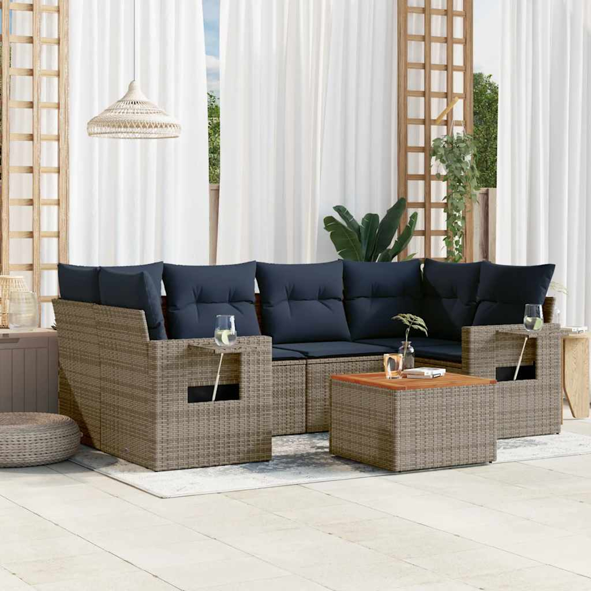 Terrassenset mit blauen Kissen, einem Couchtisch und Gläsern. Weiße Vorhänge im Hintergrund. Pflanzen und Holzstrukturen.