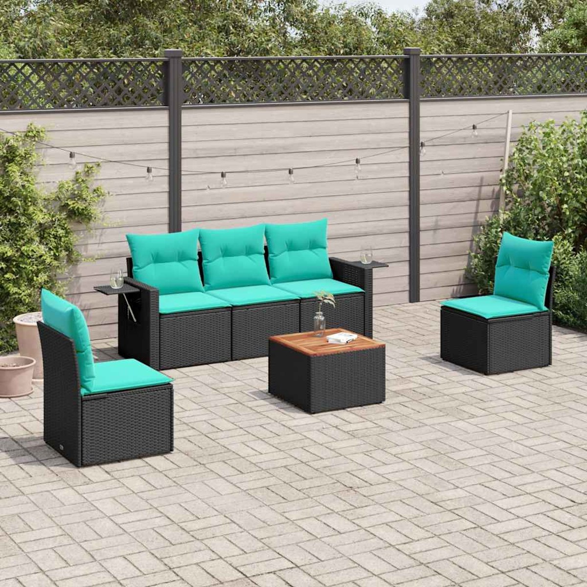 Juego de patio al aire libre con muebles de mimbre negros, cojines turquesa y mesa de centro de madera, sobre un patio pavimentado con una valla de fondo.