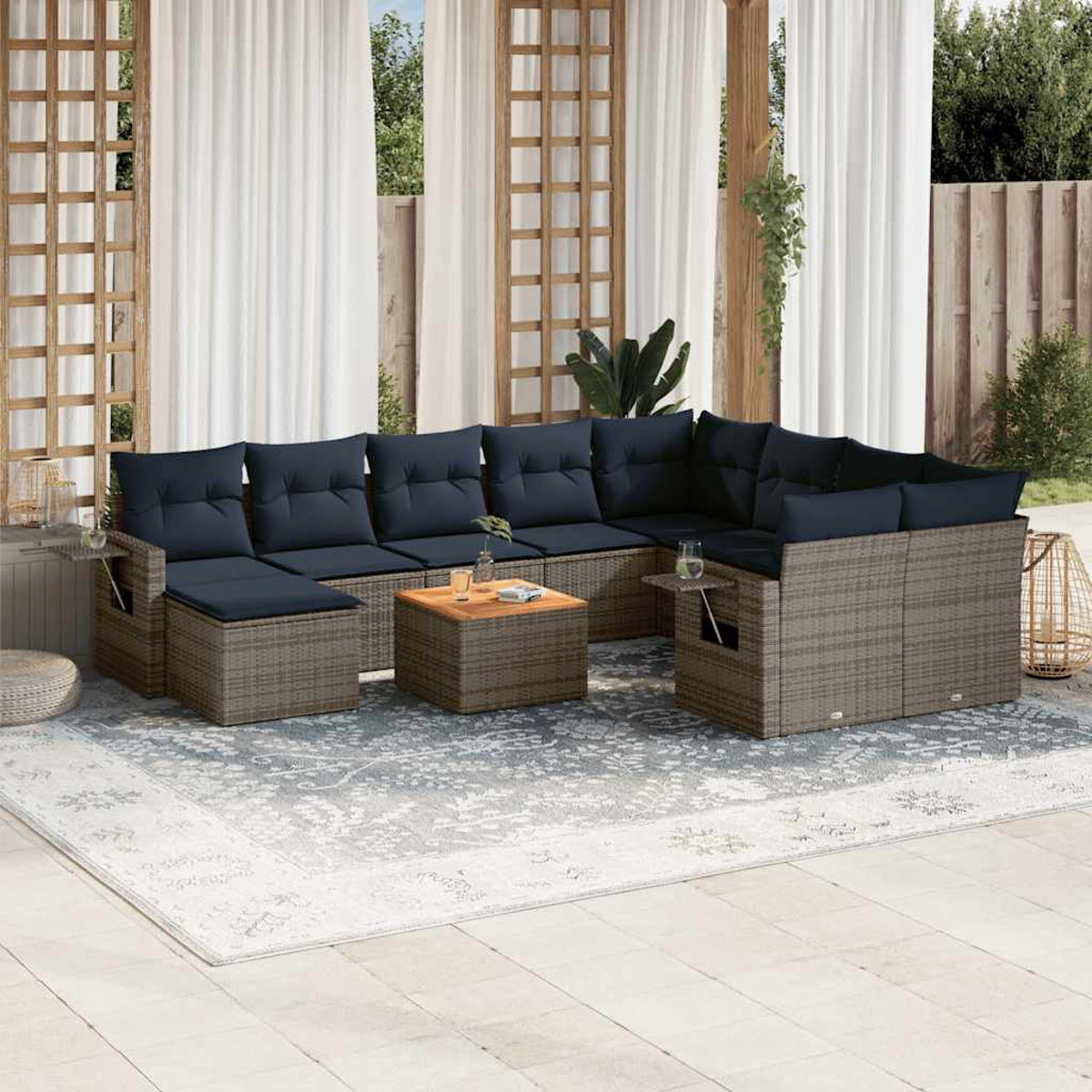 Gartensitzgruppe mit blauen Kissen und einem Holztisch. Weiße Vorhänge und Spalier im Hintergrund. Ein Teppich auf der Terrasse.