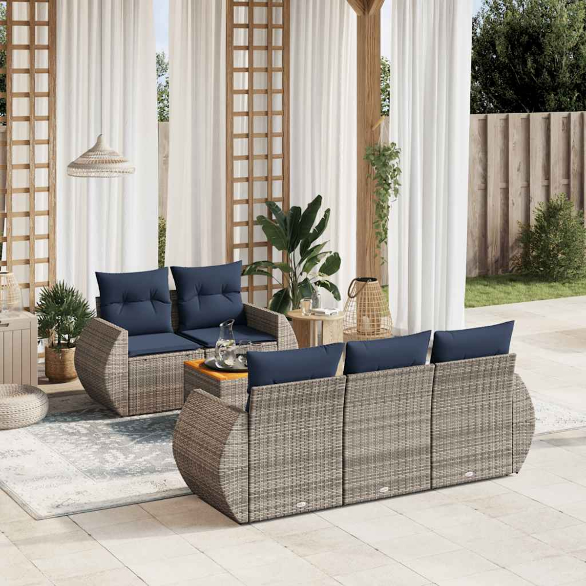 Outdoor-Sitzbereich mit Korbmöbeln, blauen Kissen, weißen Vorhängen und Pflanzen. Szene ist gut beleuchtet mit Terrasse und Garten im Hintergrund.