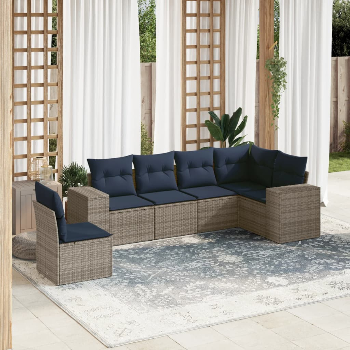 Outdoor-Sitzbereich mit einem geflochtenen Ecksofa und Stuhl, marinefarbenen Kissen, einem gemusterten Teppich und weißen Vorhängen.