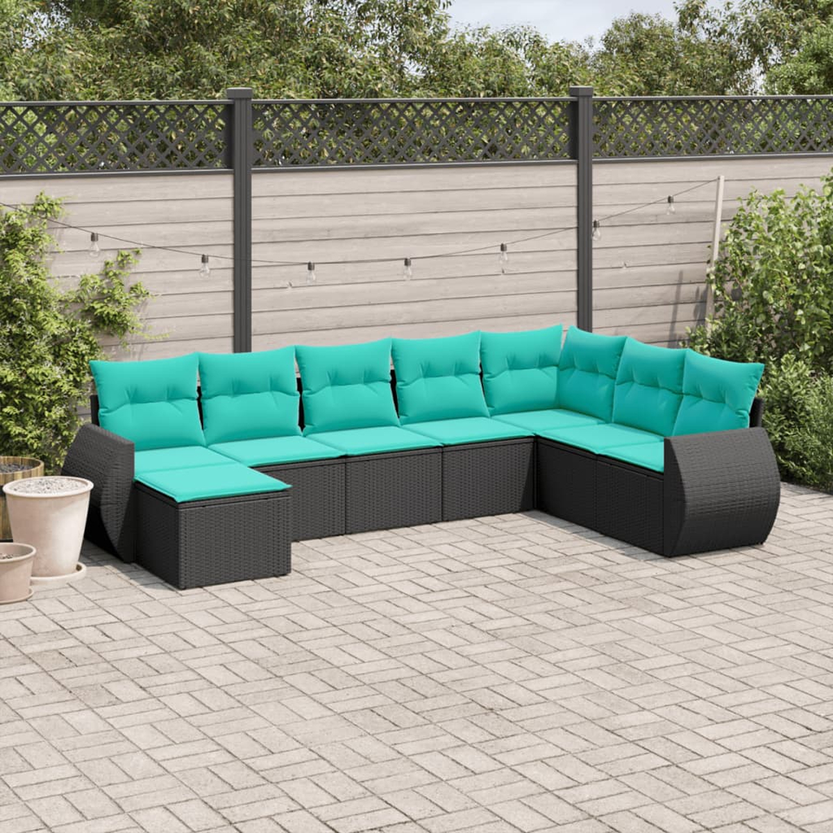 Outdoor-Ecksofa mit schwarzem Korbgewebe und türkisfarbenen Kissen auf einer Backstein-Terrasse. Grüne Pflanzen und ein Zaun sind im Hintergrund.