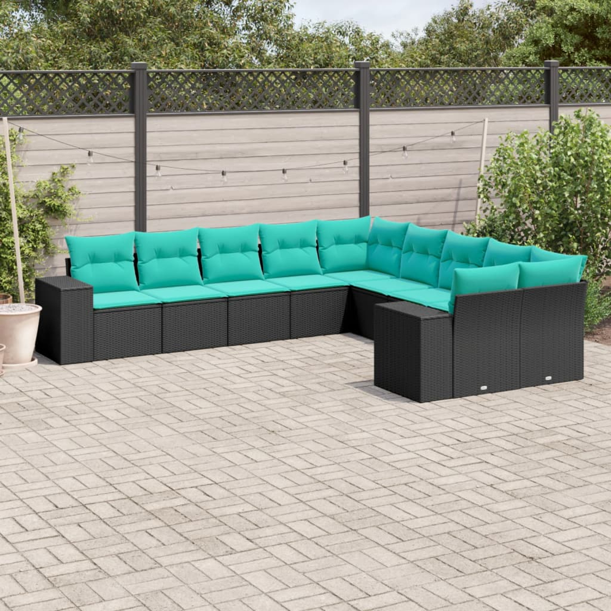 Ein Ecksofa für den Außenbereich mit schwarzem Korbgeflecht und türkisfarbenen Kissen steht auf einer Ziegelterrasse. Ein Zaun und Grünzeug sind im Hintergrund.