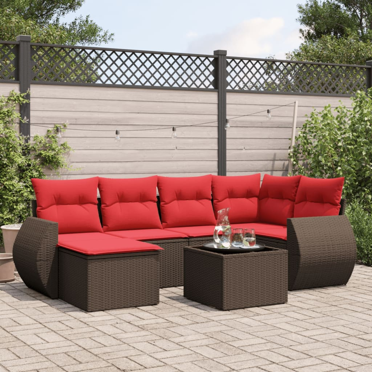Outdoor-Ecksofa mit roten Kissen und einem kleinen Tisch. Der Hintergrund zeigt einen Zaun, Pflanzen und Lichterketten.