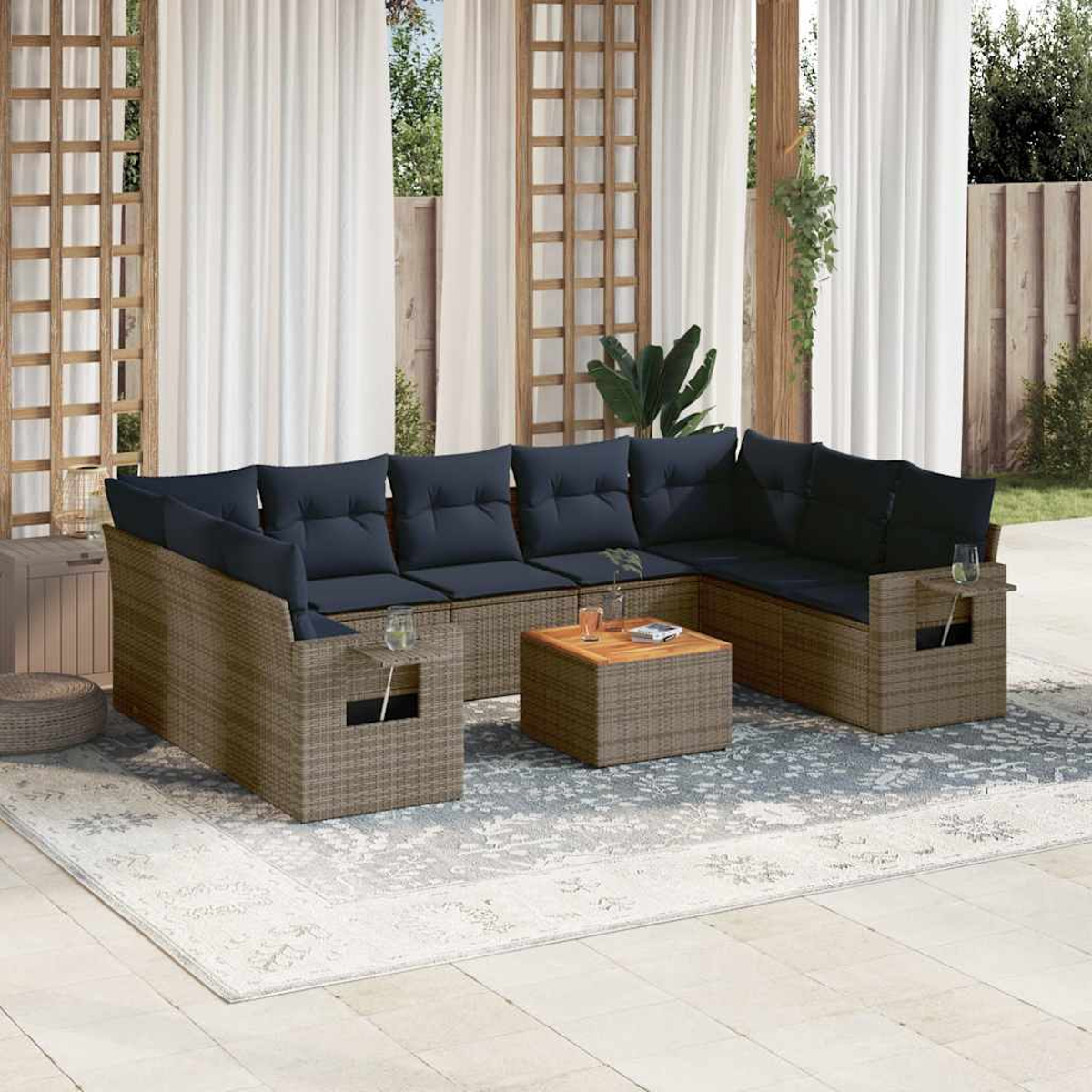 Sofá seccional exterior con cojines azul marino. Una pequeña mesa de madera y una alfombra al frente. Cortinas blancas y una valla de madera al fondo.