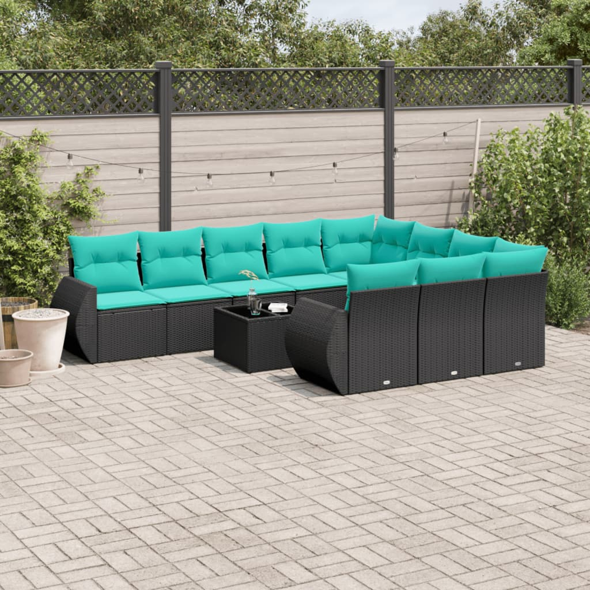 Outdoor-Ecksofa mit türkisfarbenen Kissen. Schwarze Korbmöbel auf einer Steinterrasse. Ein kleiner Tisch und Topfpflanzen sind sichtbar.