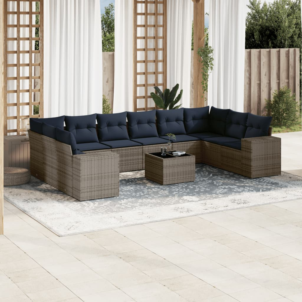 Outdoor-Sitzgruppe mit blauen Kissen auf einem gewebten braunen Sofa, einem kleinen Tisch und einem gemusterten Teppich auf einer Terrasse.
