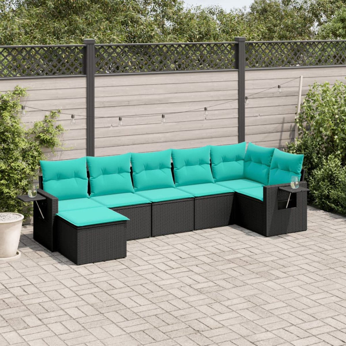 Outdoor-Ecksofa mit türkisfarbenen Kissen auf einer gepflasterten Terrasse. Ein Holzzaun und Grünzeug sind im Hintergrund.