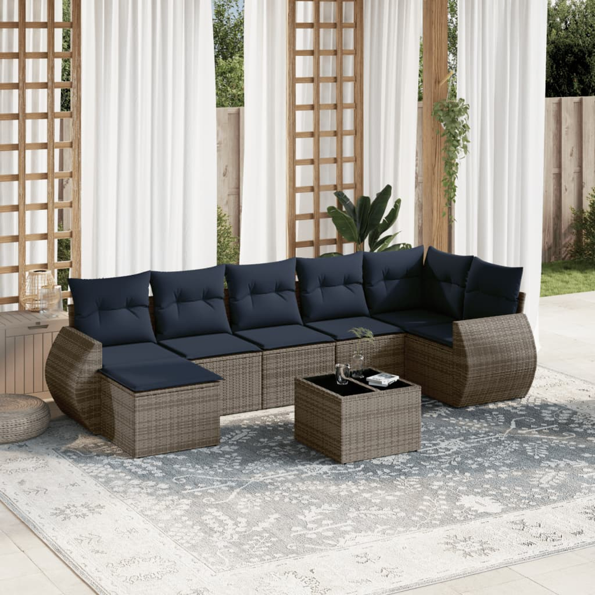 Ecksofa im Freien mit blauen Kissen und einem Couchtisch auf einem gemusterten Teppich. Weiße Vorhänge im Hintergrund, Holzstruktur.