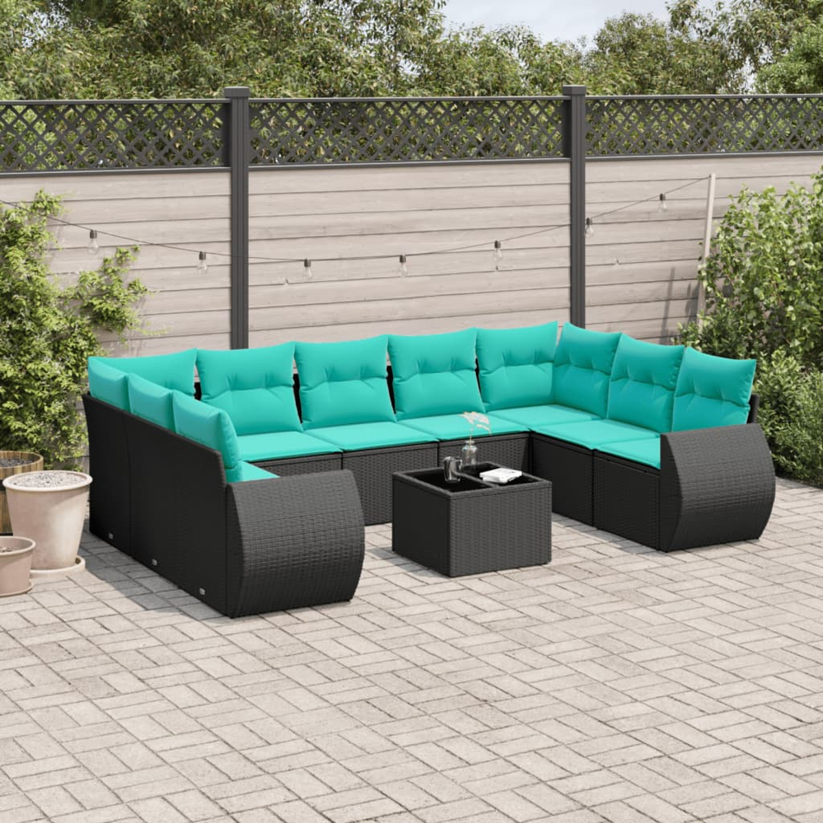 Ein Ecksofa im Freien mit türkisfarbenen Kissen und einem schwarzen Couchtisch steht auf einer Ziegelterrasse. Im Hintergrund sind ein Zaun und Grün.