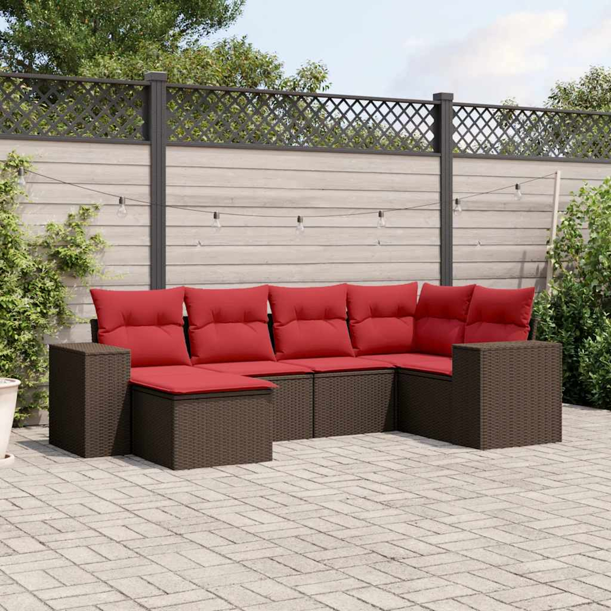 Outdoor-Ecksofa mit roten Kissen auf einer Ziegelterrasse. Im Hintergrund ein Holzzaun und Grün.