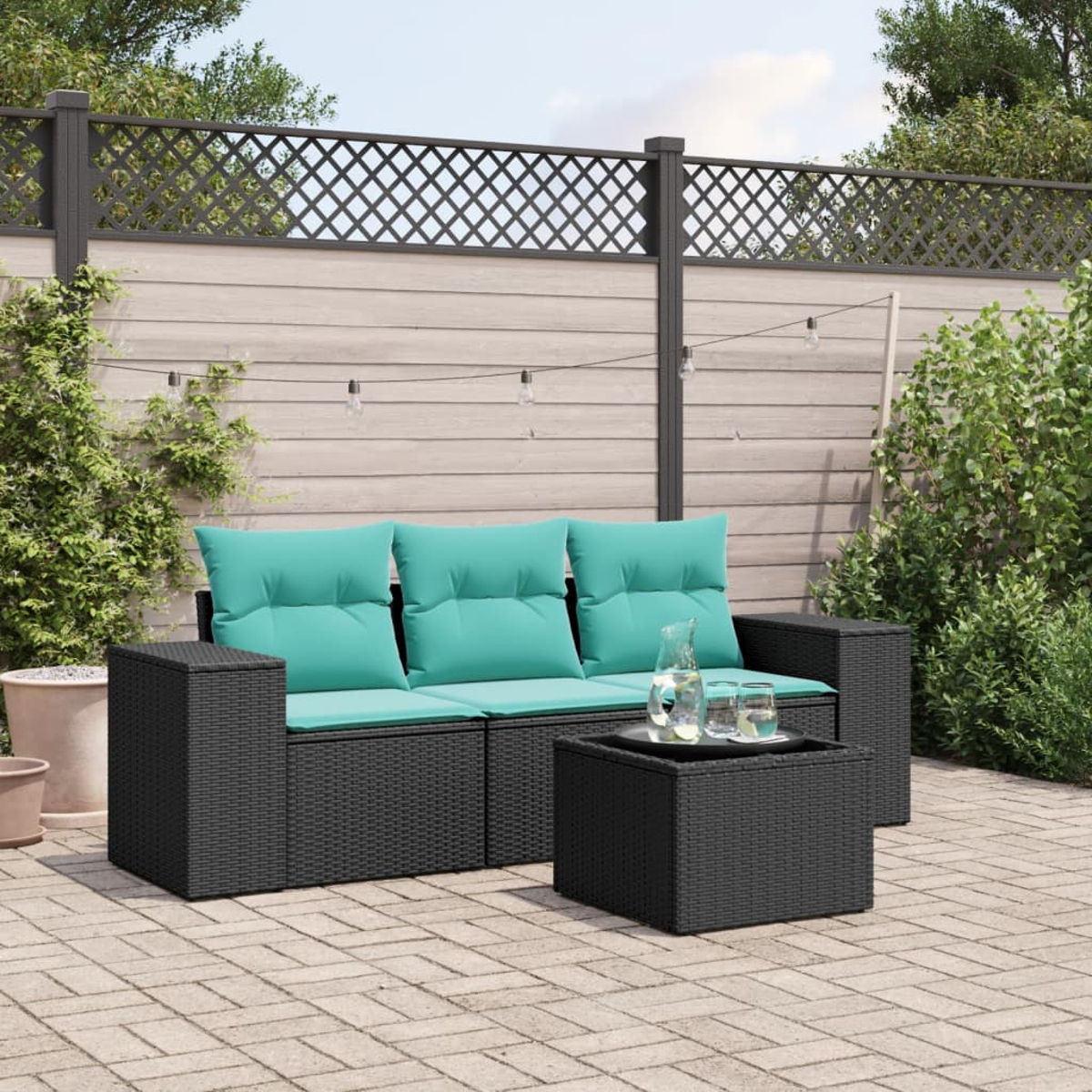 Garten-Sofa-Set mit schwarzem Rattansofa, türkisfarbenen Kissen und passendem Couchtisch. Hintergrund: Zaun und Grün.