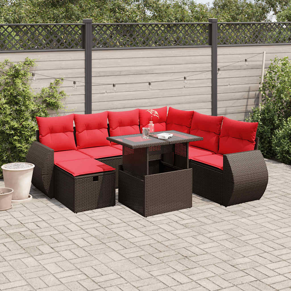 Garten-Ecksofa mit roten Kissen und Glastisch. Auf einer Ziegelterrasse, mit Zaun und Grün im Hintergrund.
