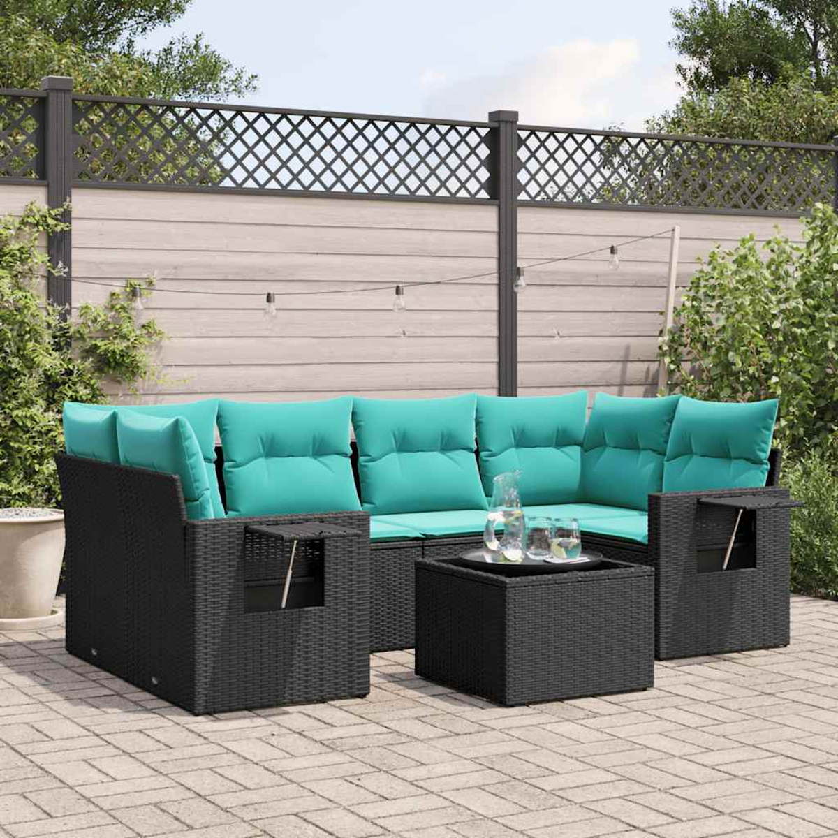 Garten-Sitzgruppe: schwarzes Korbmöbel mit türkisfarbenen Kissen, kleiner Tisch. Hintergrund: Holzzaun, Pflanzen und Lichterketten.