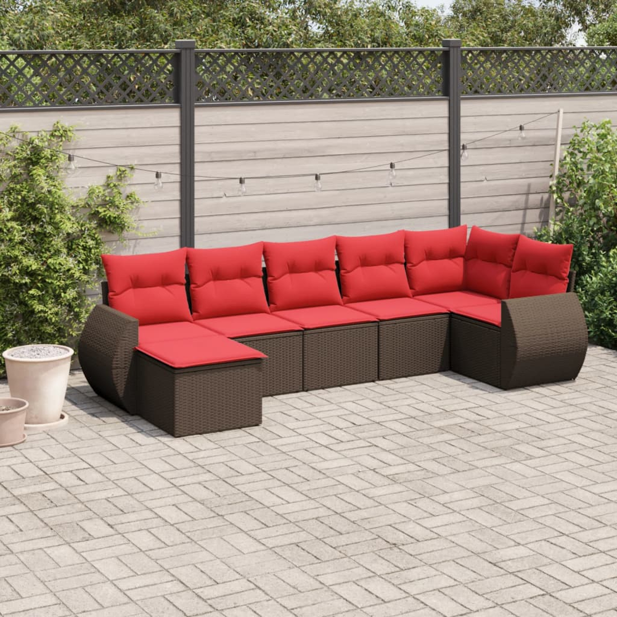 Outdoor-Ecksofa mit roten Kissen auf einer Backstein-Terrasse. Im Hintergrund ein Zaun, Pflanzen und Lichterketten.