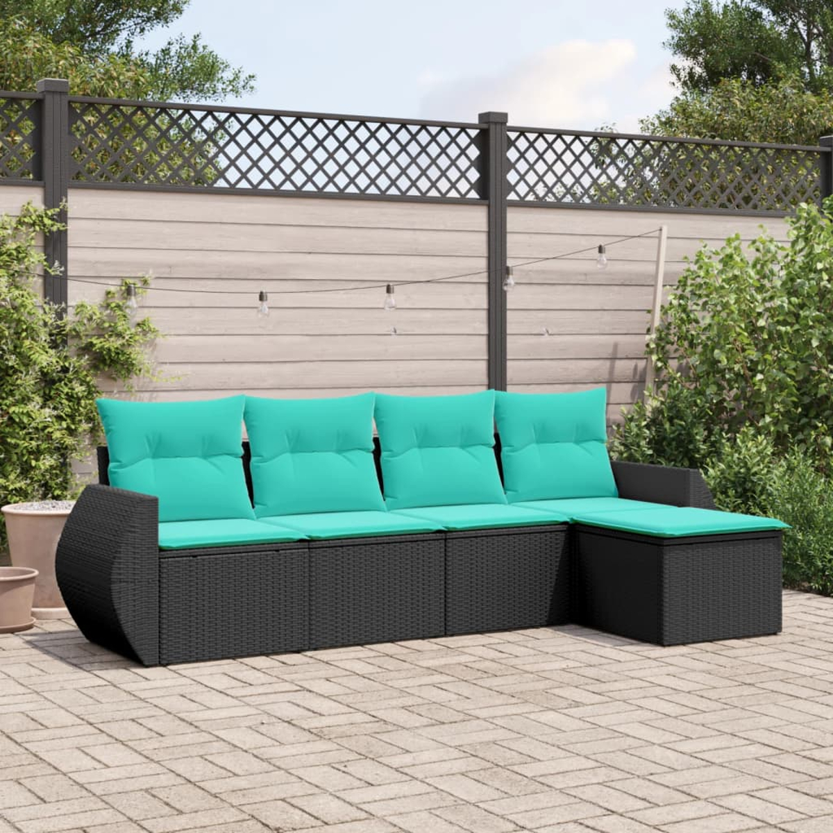 Ein schwarzes Outdoor-Ecksofa aus Korbgeflecht mit türkisfarbenen Kissen steht auf einer Ziegelpflasterung. Hintergrund: Zaun und Grün.