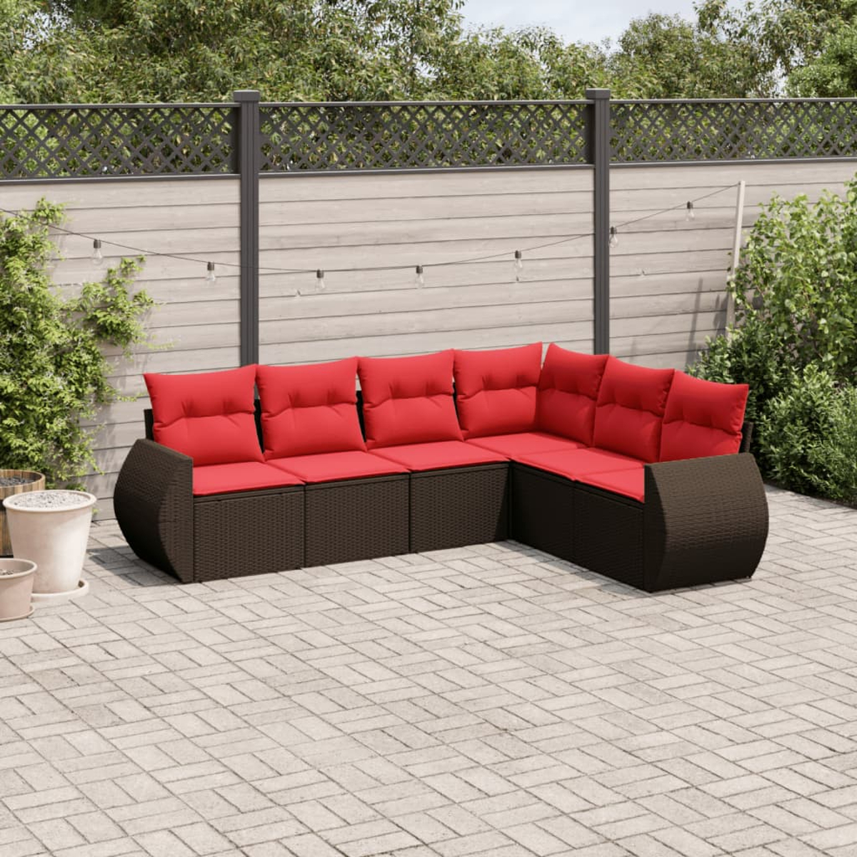 Ein Ecksofa mit roten Kissen im Freien steht auf einer Ziegelterrasse. Im Hintergrund befinden sich ein Zaun und Grün.