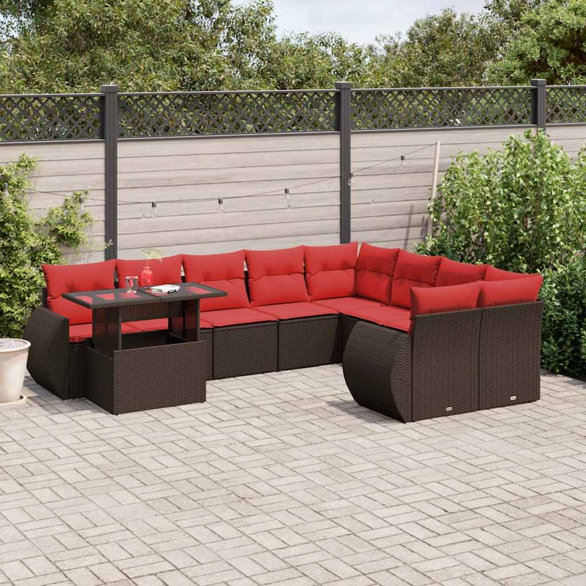 Garten-Sitzgruppe mit roten Kissen und einem Tisch mit Glasplatte. Braune Korbmöbel auf einer Terrasse, mit Zaun und Grün im Hintergrund.