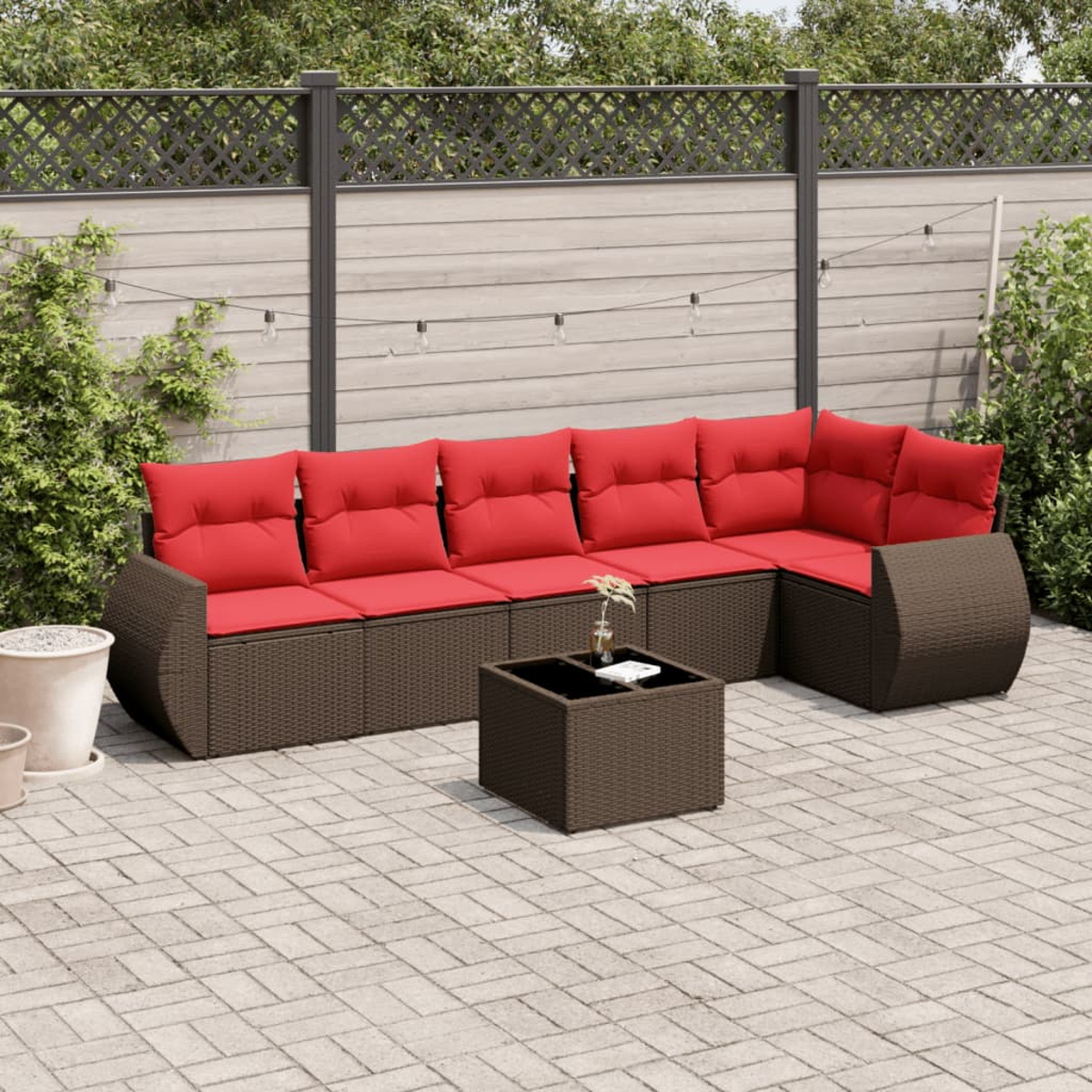 Ecksofa im Freien mit roten Kissen und einem quadratischen Couchtisch auf einer Ziegelterrasse. Hintergrund umfaßt Zaun und Grün.