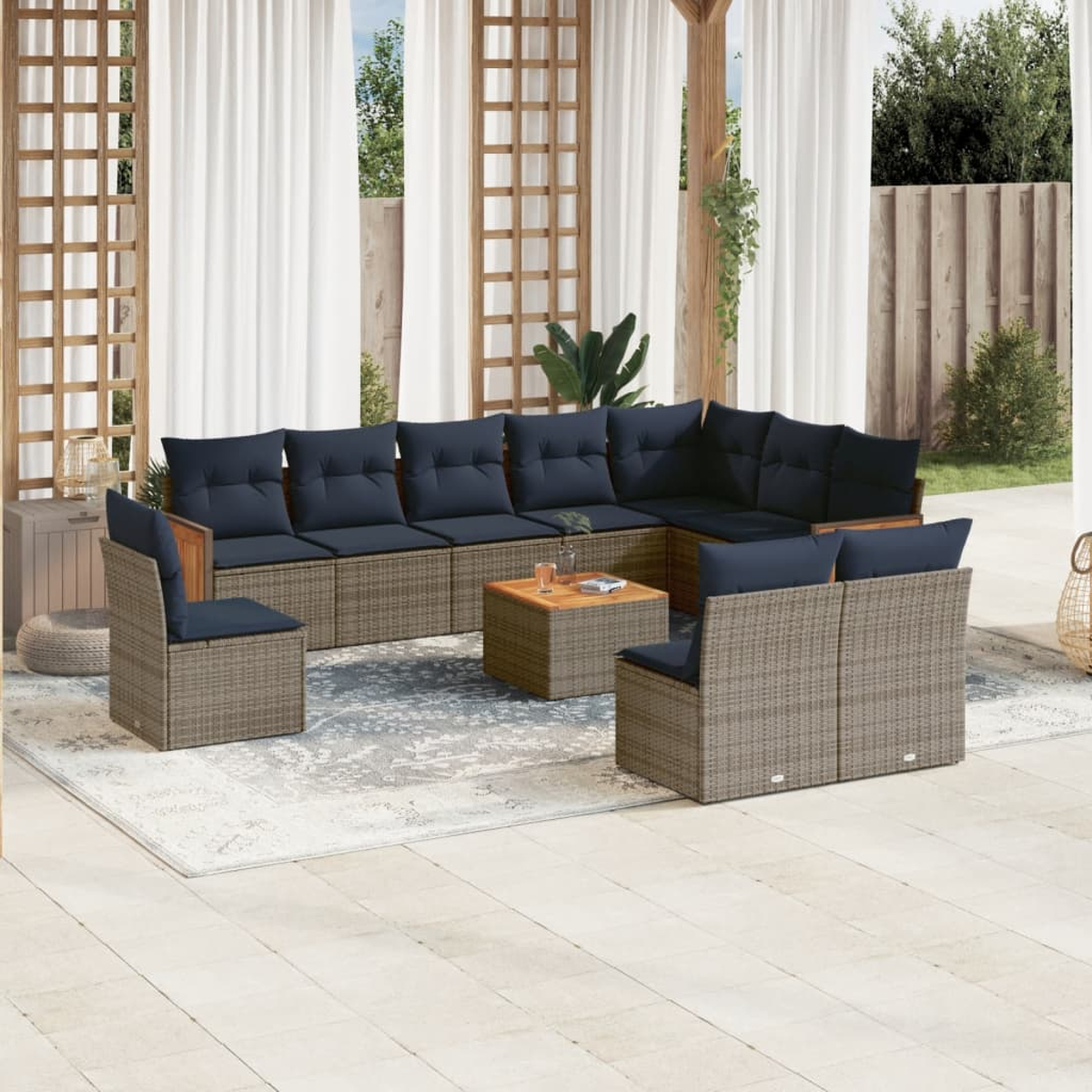 Juego de muebles de patio exterior. Sofás de mimbre gris con cojines azul marino sobre una alfombra. En el fondo, celosía de madera y cortinas.