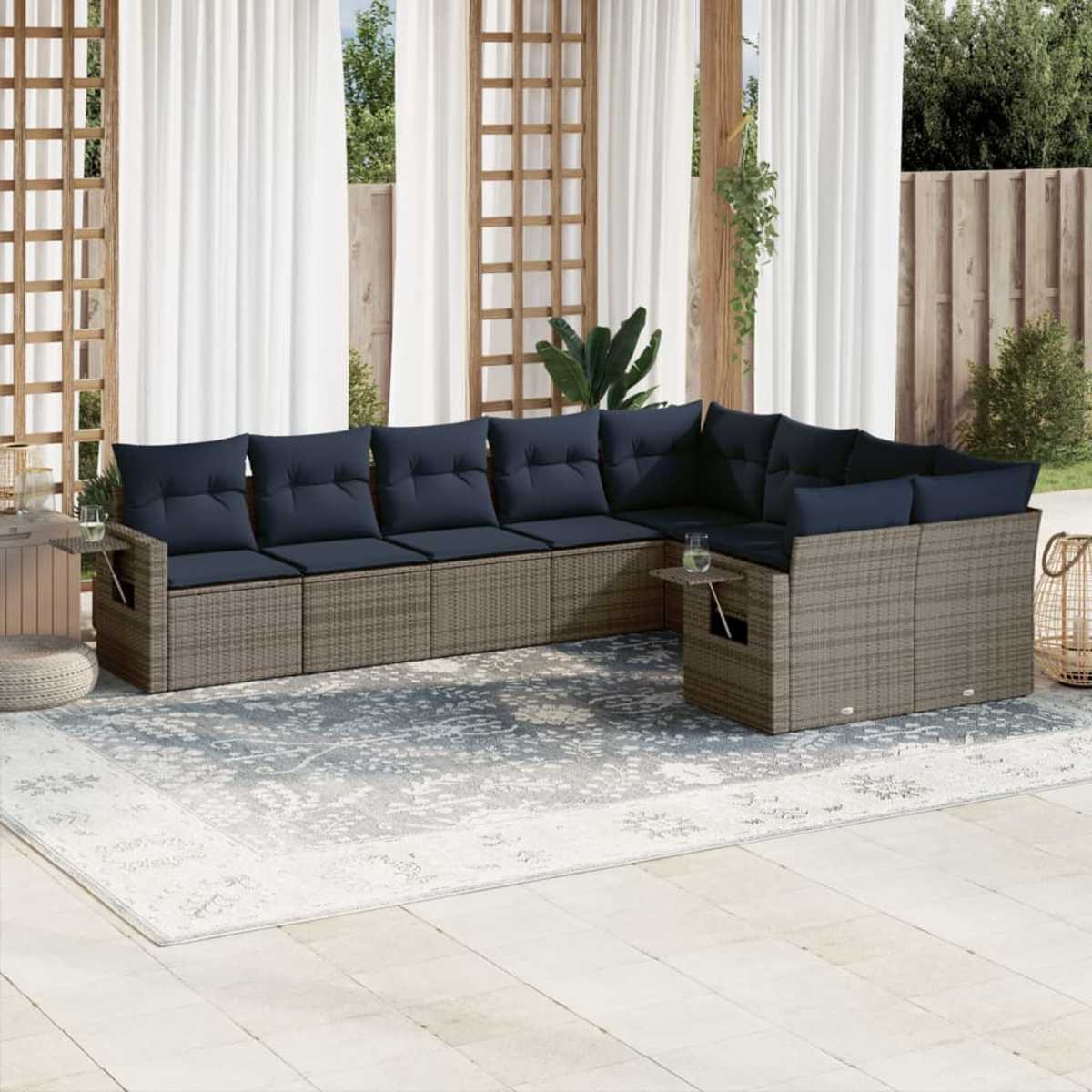 Ein Ecksofa im Freien mit blauen Kissen steht auf einem gemusterten Teppich. Weiße Vorhänge und Holzgitter im Hintergrund.