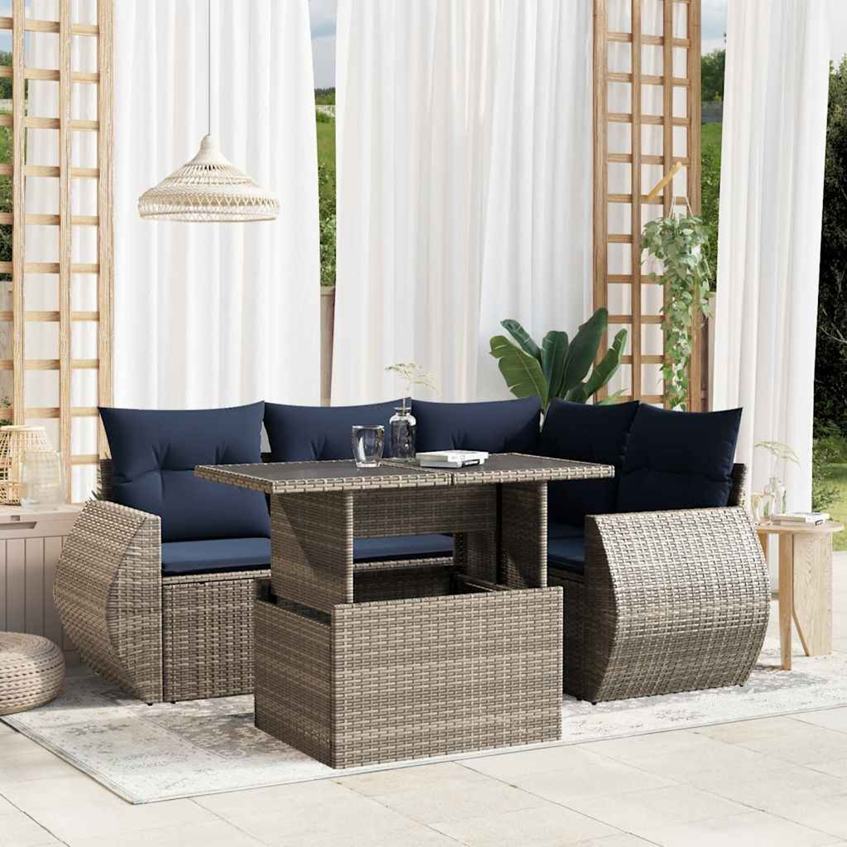 Garten-Sitzgruppe mit einem gewebten Tisch und Sofa mit blauen Kissen. Weiße Vorhänge und eine Hängelampe sind sichtbar.