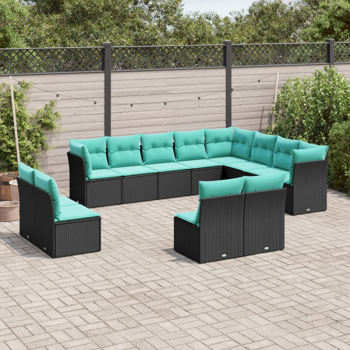 Outdoor-Ecksofa-Set mit schwarzen Korbflechtrahmen und türkisfarbenen Kissen auf einer gepflasterten Terrasse. Im Hintergrund ein Holzzaun und Grün.