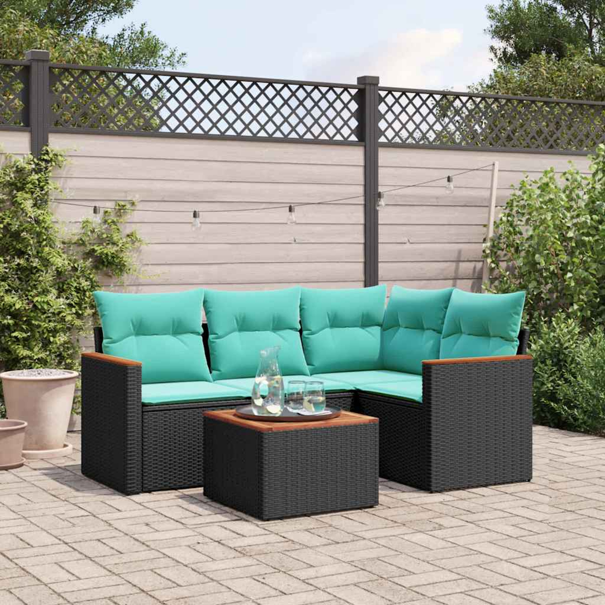 Garten-Terrassenset mit schwarzem Korbsessel, türkisfarbenen Kissen und Couchtisch. Hintergrund hat Holzzaun und Grün.