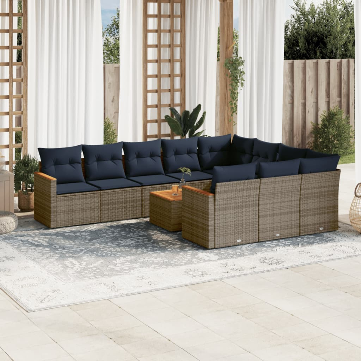 Outdoor-Ecksofa mit blauen Kissen und einem Holztisch. Beige Korbmöbel auf einer Terrasse mit Teppich und weißen Vorhängen.